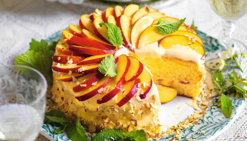 Torta di pesche morbidissima, decorata con fettine di pesca, mandorle e menta. Un dolce estivo invitante.