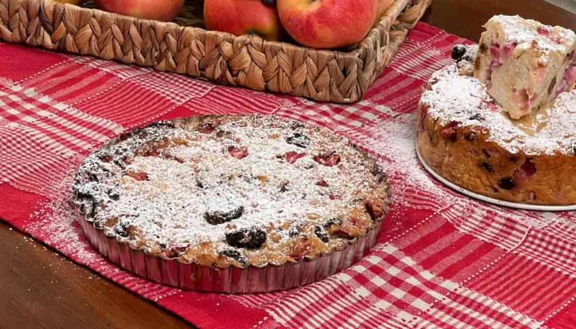 Una torta putana, ricca di frutta e spolverata di zucchero a velo, su una tovaglia a quadri rossi.