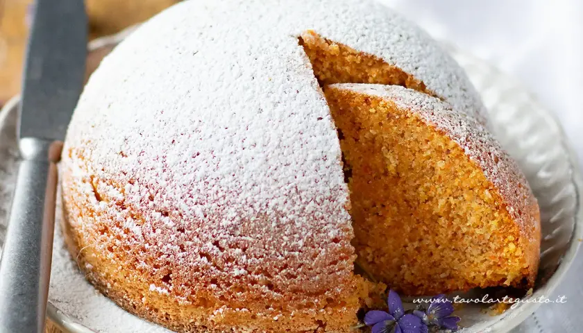 Torta Camilla ricetta originale: soffice torta cosparsa di zucchero a velo, con una fetta tagliata che rivela l'interno dorato e profumato.