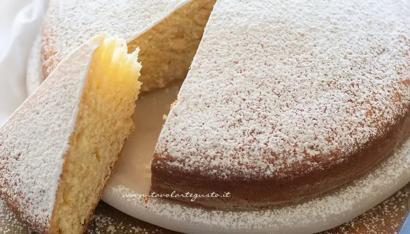 Torta soffice senza uova, cosparsa di zucchero a velo, con una fetta tagliata che ne mostra l'interno dorato.