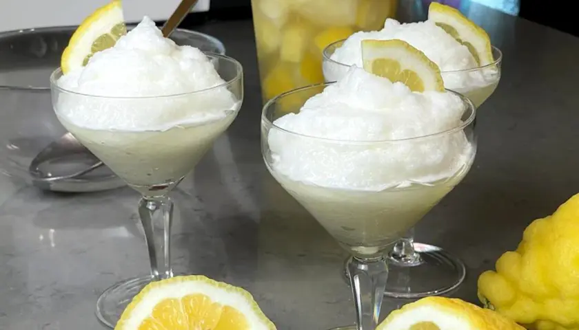 Tre coppe di granita al limone, guarnite con fette di limone, pronte per essere gustate. La ricetta granita al limone è perfetta per rinfrescarsi.