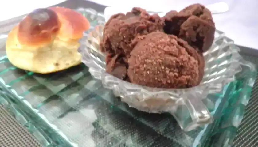 Un dolce pane intrecciato accanto a una coppa di granita cioccolato, serviti su un piatto di vetro.