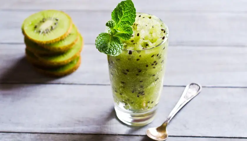 Sorbetto al kiwi rinfrescante, guarnito con menta, accanto a fette di kiwi impilate e un cucchiaino.