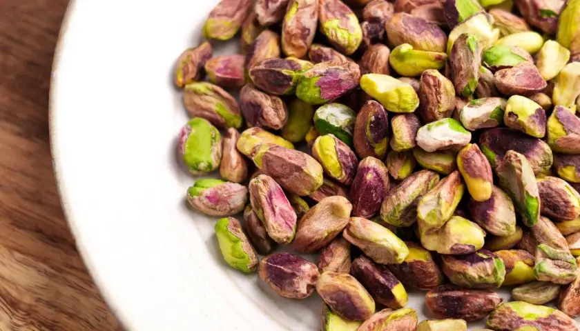 Pistacchi sgusciati su un piatto bianco, un assaggio di dove cresce il pistacchio in Italia, con i loro colori verdi e viola.