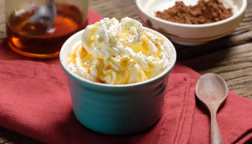 Dolcezza cremosa: cos'è heavy cream? Panna montata soffice, caramello dorato e una spolverata di cacao su un tavolo rustico.