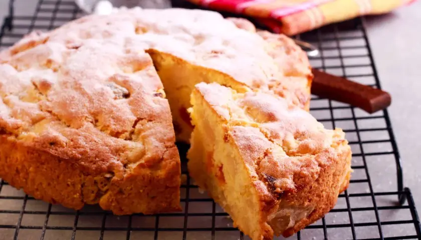 Una fetta di torta albicocche, cosparsa di zucchero a velo, riposa su una griglia.