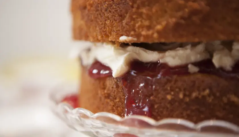 Torta soffice con panna e tanta marmellata di fragole che cola, servita su un piatto di cristallo.