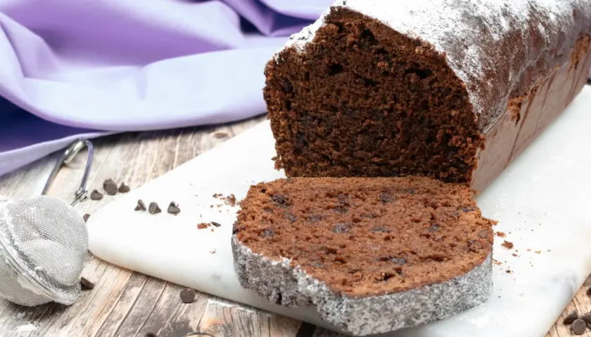 Plumcake al cioccolato soffice e goloso, spolverato di zucchero a velo, con gocce di cioccolato visibili.