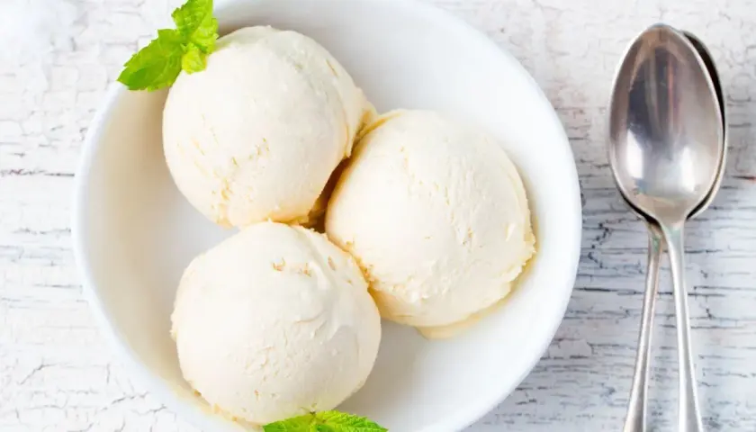 Tre palline di gelato alla vaniglia in una ciotola bianca, guarnite con menta. Perfetto per scoprire come rendere cremoso il gelato fatto in casa.