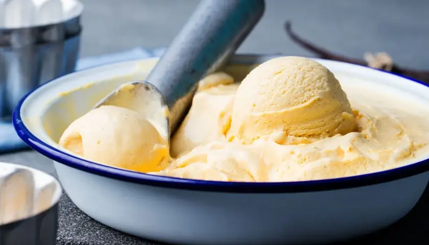 Ciotola di gelato alla vaniglia fatto in casa, con palline cremose e un mestolo. Perfetto per una calda giornata estiva.
