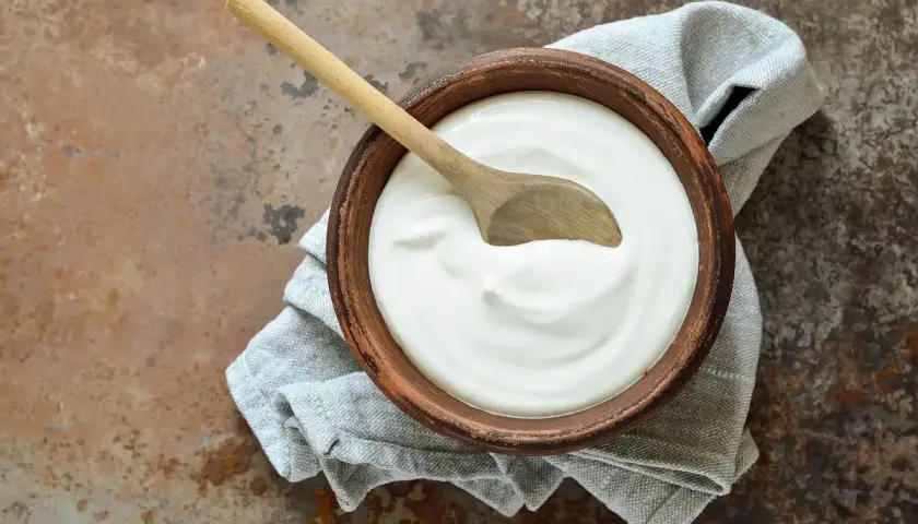 Ciotola di terracotta con panna fresca e cucchiaio di legno, un'idea su come si fa la panna da cucina in casa.