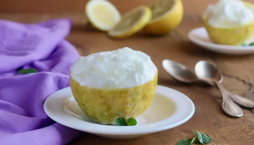 Sorbetto al limone ricetta: un fresco dessert servito in un limone svuotato, con limoni affettati e menta sullo sfondo.