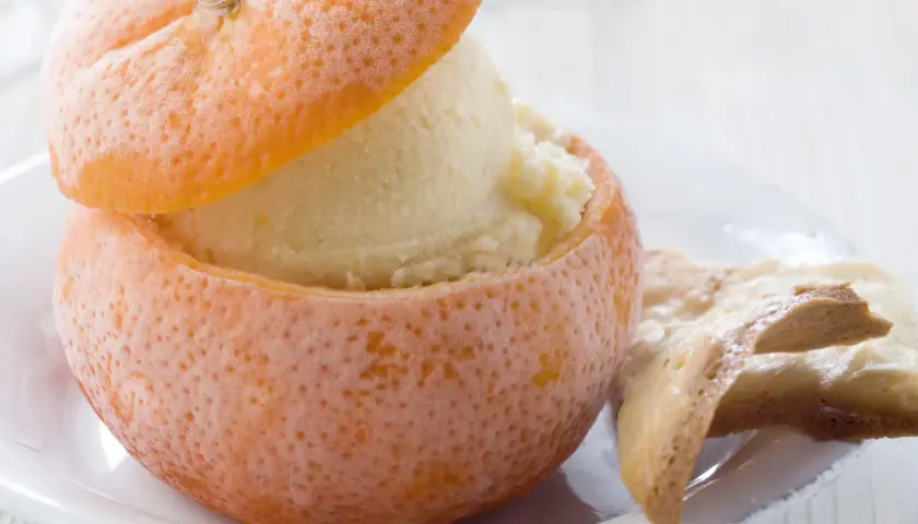 Sorbetto all'arancia servito in una scorza d'arancia ghiacciata, accompagnato da biscotti croccanti.