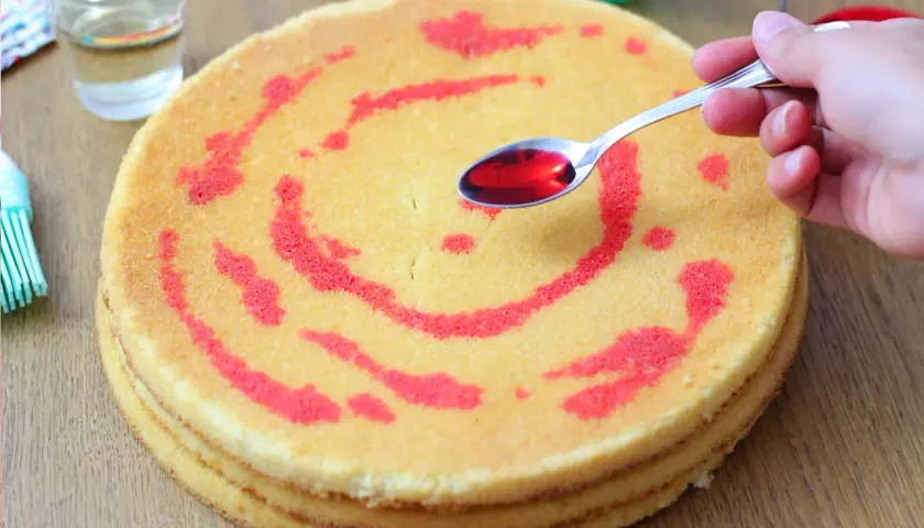 Un cucchiaino di sciroppo rosso viene versato su un pan di spagna a strati, decorato con un motivo a spirale.