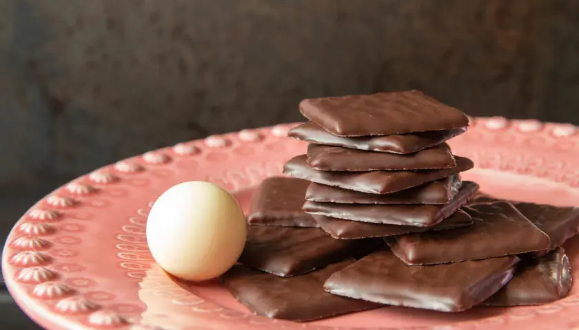 Piatto rosa con cioccolatini quadrati al cioccolato fondente e una pallina bianca. Un invito al gusto after eight.
