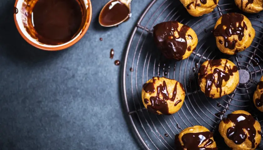 Profitterol ricetta: bignè dorati glassati con cioccolato fuso, pronti per essere gustati.
