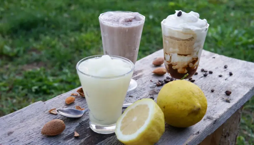 Tre granite siciliane, una al limone, preparate con gelatiera, su un tavolo di legno con limoni e mandorle.