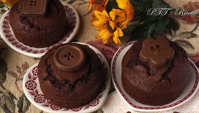 Tre deliziosi cupcake al cioccolato, decorati con bottoni di cioccolato, su piattini con fiori gialli sullo sfondo.