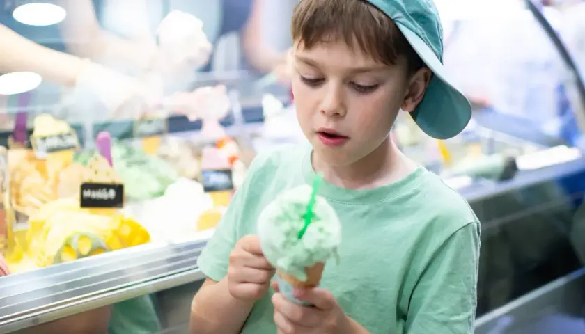 Bambino con cappellino azzurro gusta un gelato verde, pensando a chi ha inventato questa delizia.