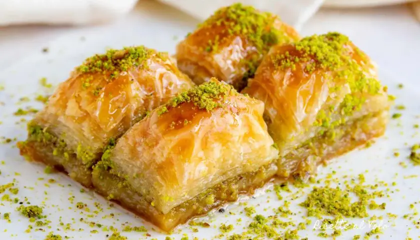 Quattro dolcetti di baklava, ricoperti di sciroppo dorato e pistacchi tritati, pronti per essere gustati.
