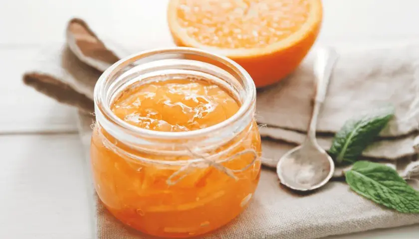 Barattolo di marmellata di arance fatto in casa, con una fetta d'arancia sullo sfondo.
