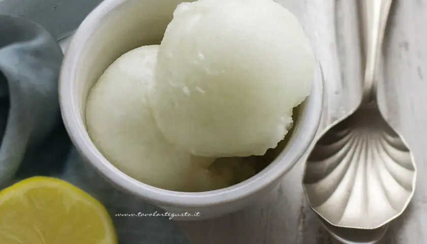 Delizioso sorbetto fatto in casa al limone, servito in una ciotola con una fetta di limone e un cucchiaio decorato.