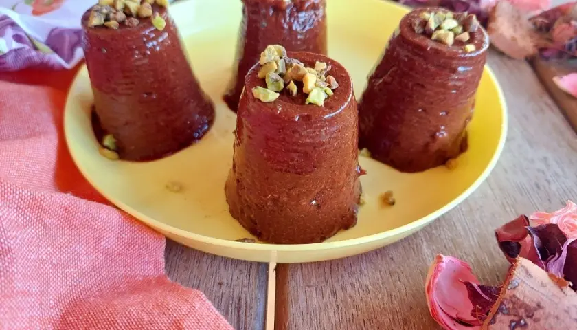 Quattro budini cachi e cacao, guarniti con pistacchi tritati, su un piatto giallo.