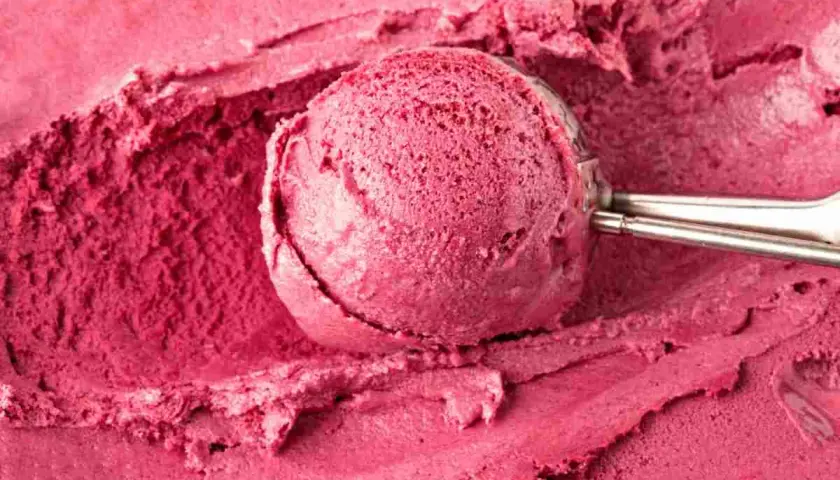Un cucchiaio raccoglie un gelato rosa intenso, cremoso e invitante, preparato con latte e frutti di bosco.