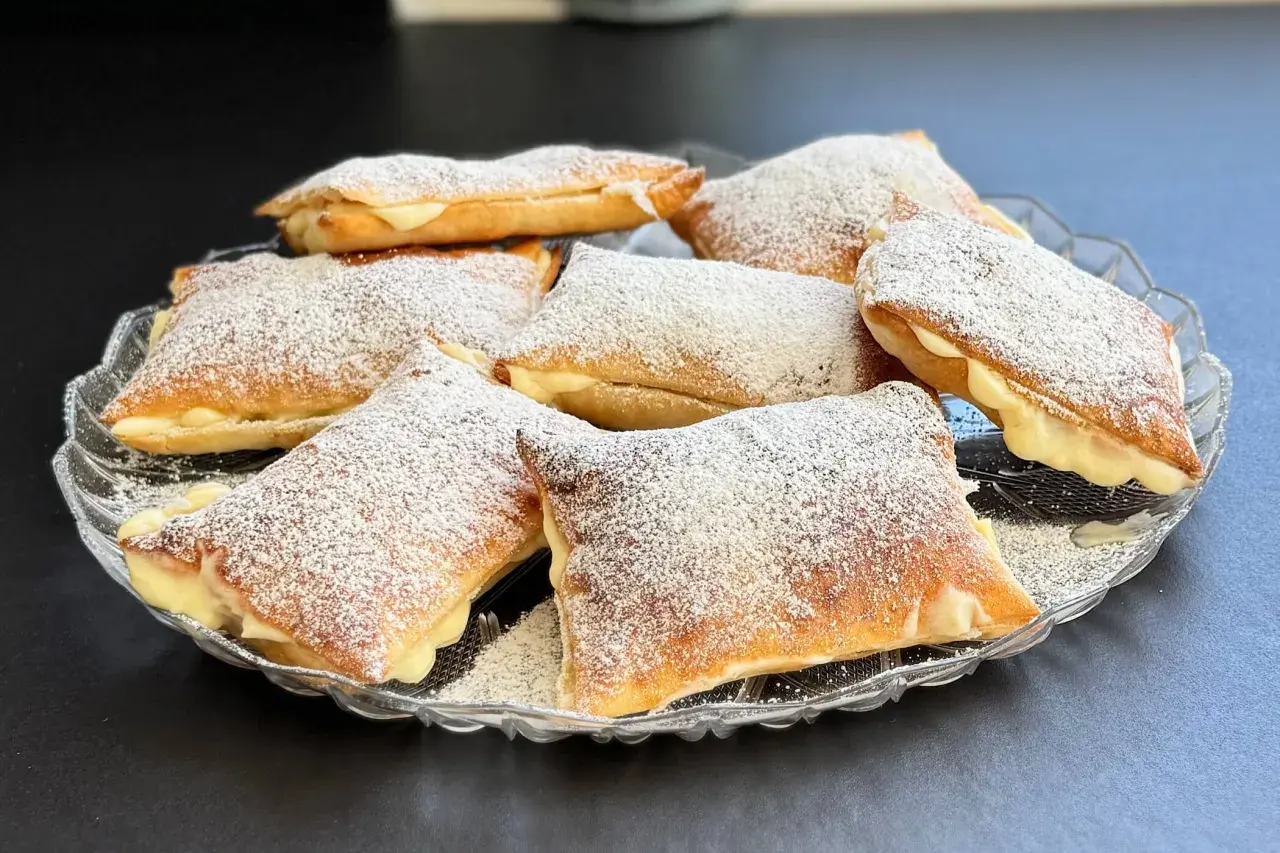 Deliziosi dolci con pasta sfoglia ripieni di crema e spolverati di zucchero a velo, serviti su un piatto di vetro.