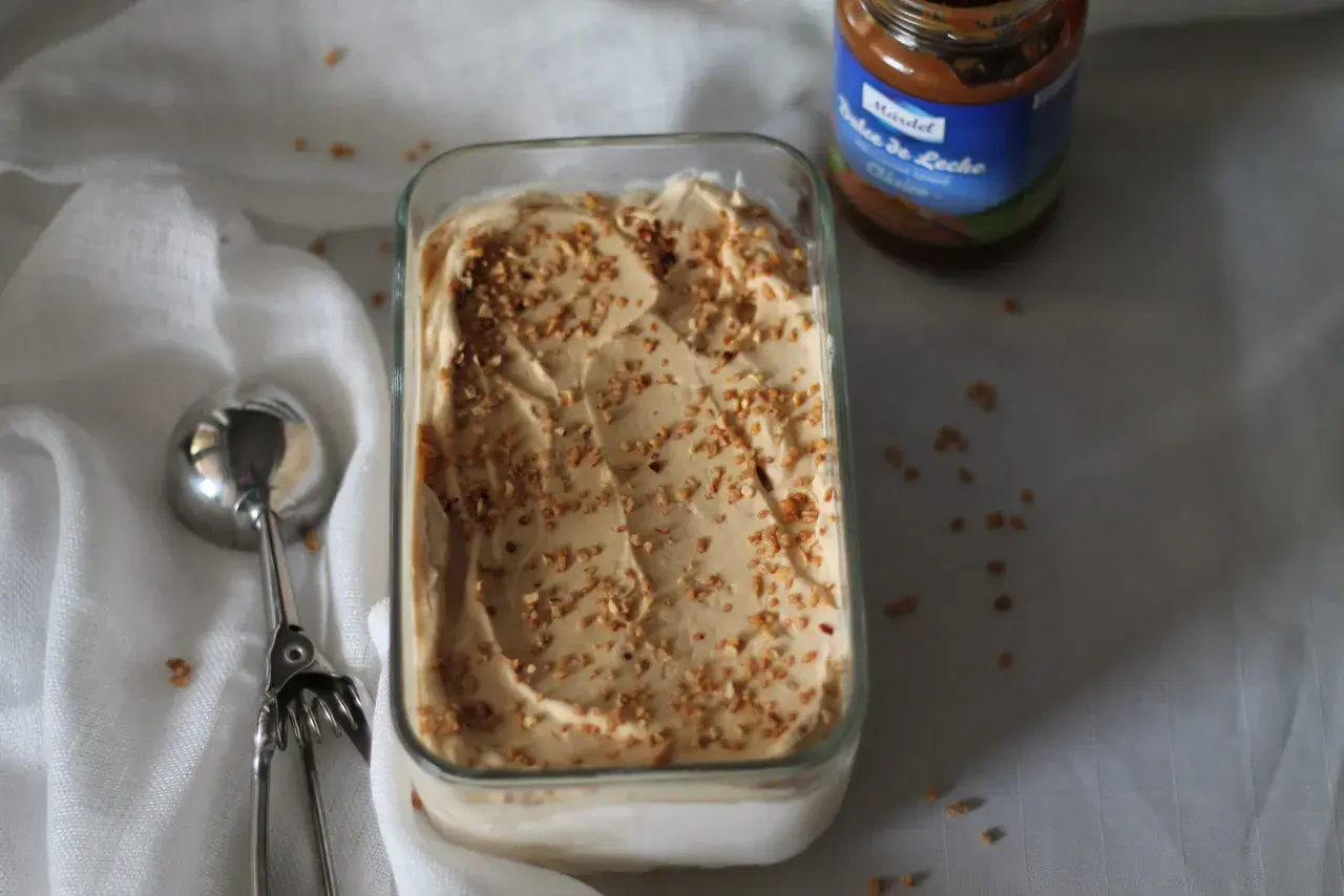 Gelato cremoso con granella di nocciole, accanto a un barattolo di dulce de leche.