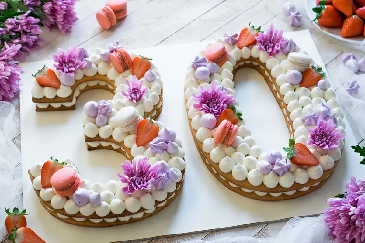 Torta numero 30 decorata con panna, fragole, macarons e fiori viola.