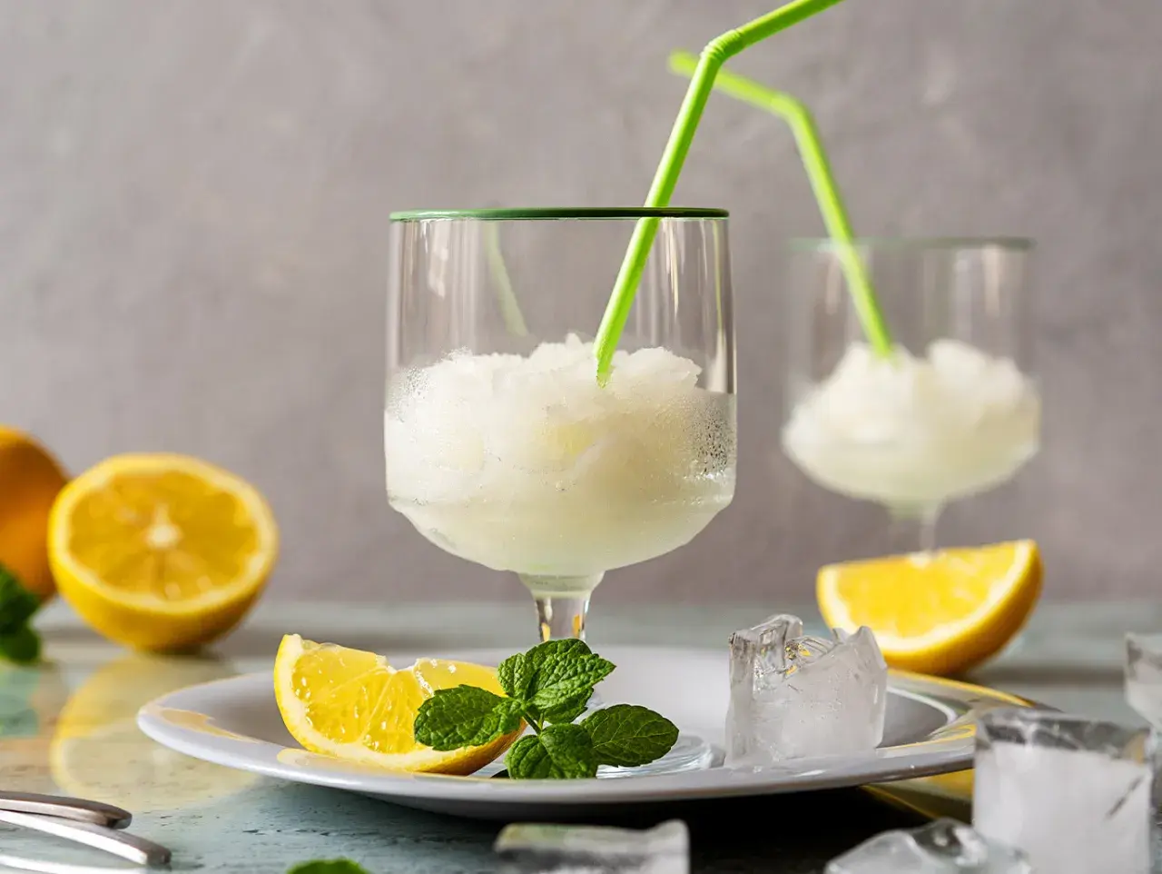 Sorbetto al limone fresco, preparato con la gelatiera, servito in bicchieri con cannucce verdi, guarnito con spicchi di limone e menta.
