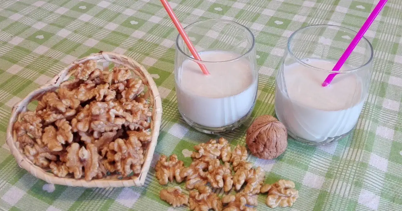 Due bicchieri con latte di noci fatto in casa, una ciotola a forma di cuore piena di noci e noci sparse sul tavolo.