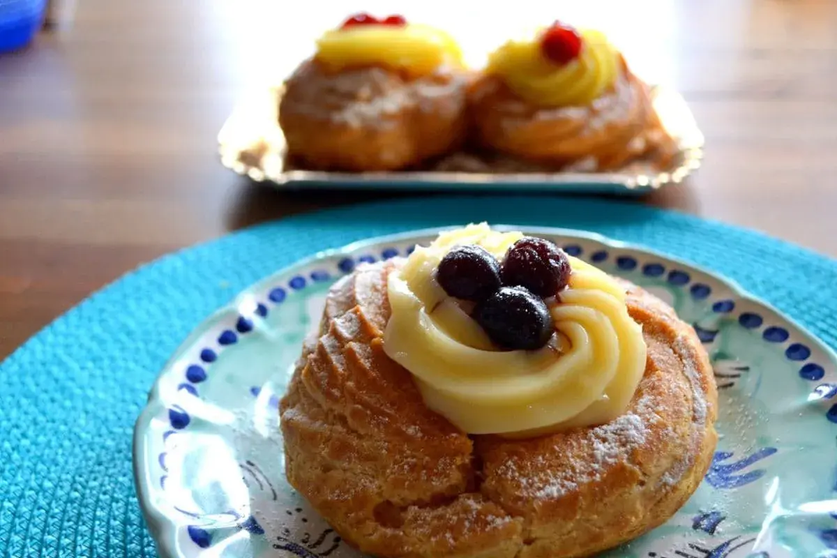 Zeppole, deliziosi dolci napoletani, guarnite con crema pasticcera e frutti di bosco su un piatto decorato.