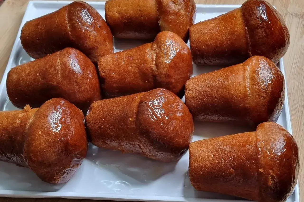 Un vassoio di baba napoletani, dolci iconici del baba Italia, dorati e lucidi di sciroppo.