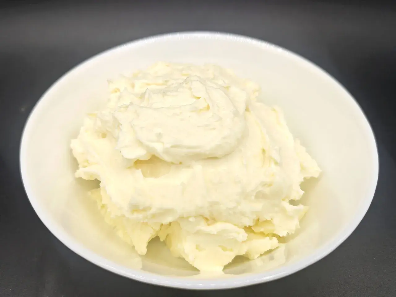 Un cremoso mascarpone fatto in casa con latte, servito in una ciotola bianca. La sua consistenza morbida e invitante promette delizie culinarie.