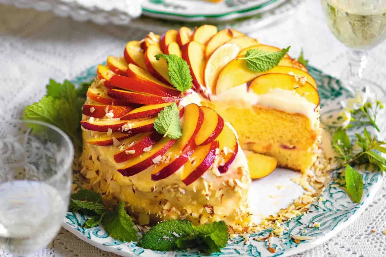 Torta di pesche morbidissima, decorata con fettine di pesca, mandorle e menta. Un dolce estivo invitante.