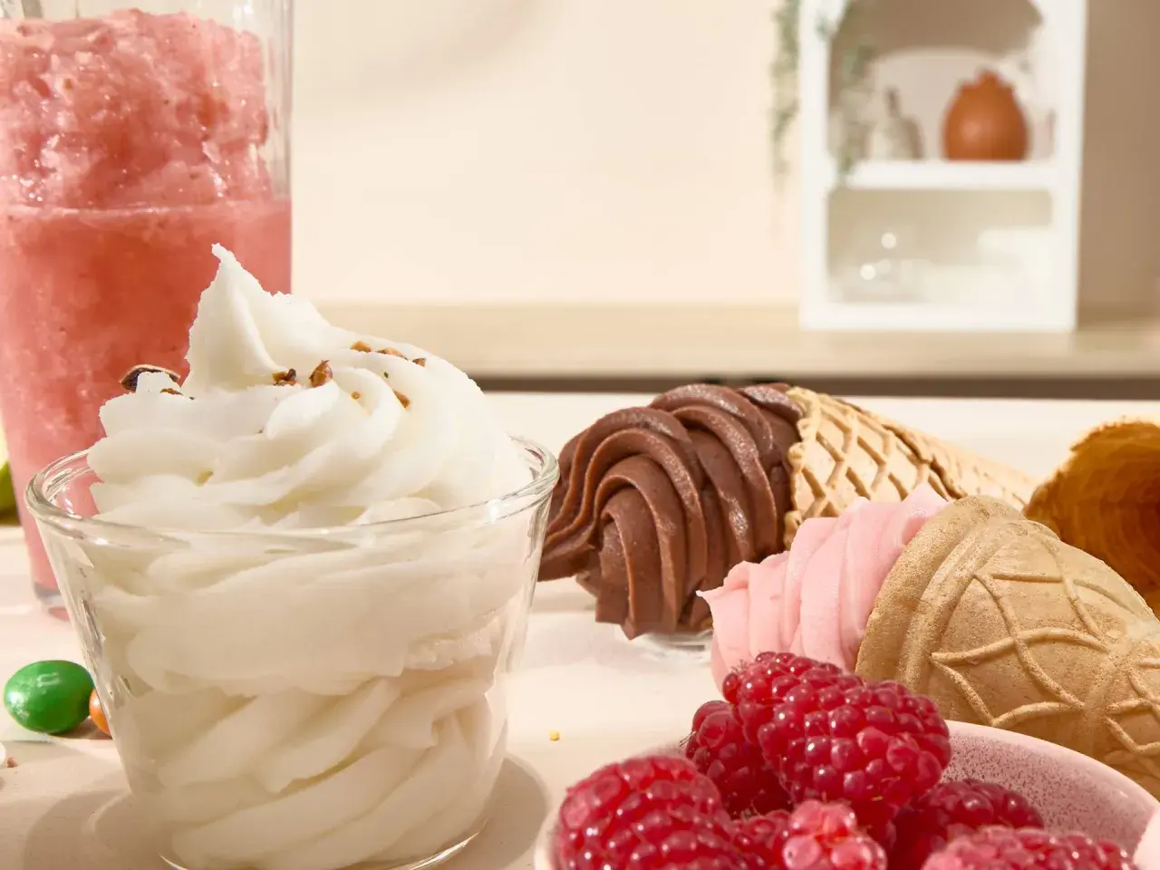 Un bicchiere di gelato sorbetto bianco, coni con gelato al cioccolato e fragola, lamponi freschi e una granita rosa.