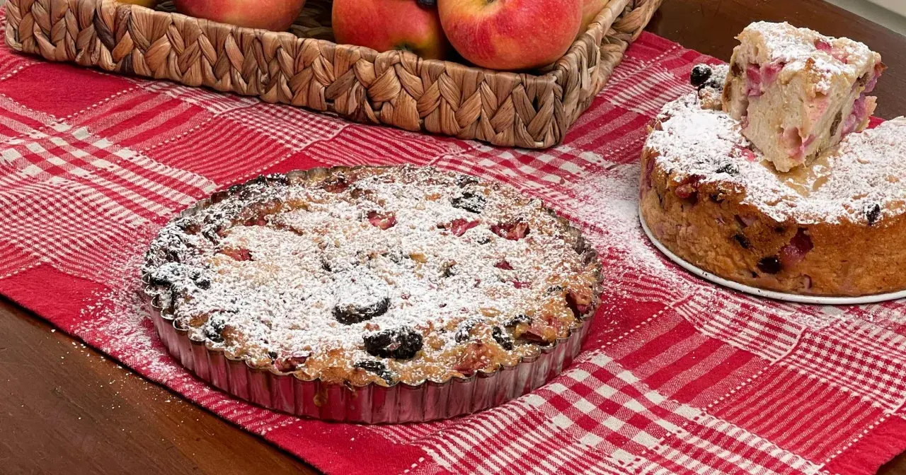 Una torta putana, ricca di frutta e spolverata di zucchero a velo, su una tovaglia a quadri rossi.
