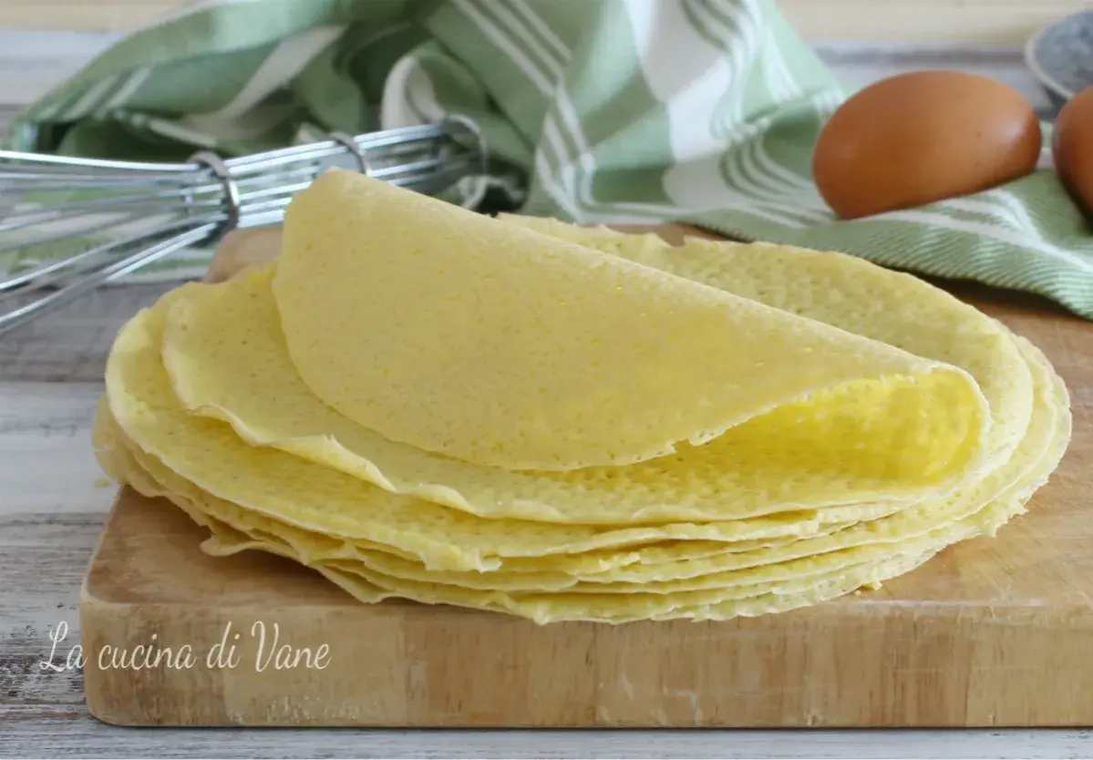 Una pila di crepes dorate su un tagliere di legno, pronte per essere farcite. La ricetta crepes perfetta per ogni occasione.