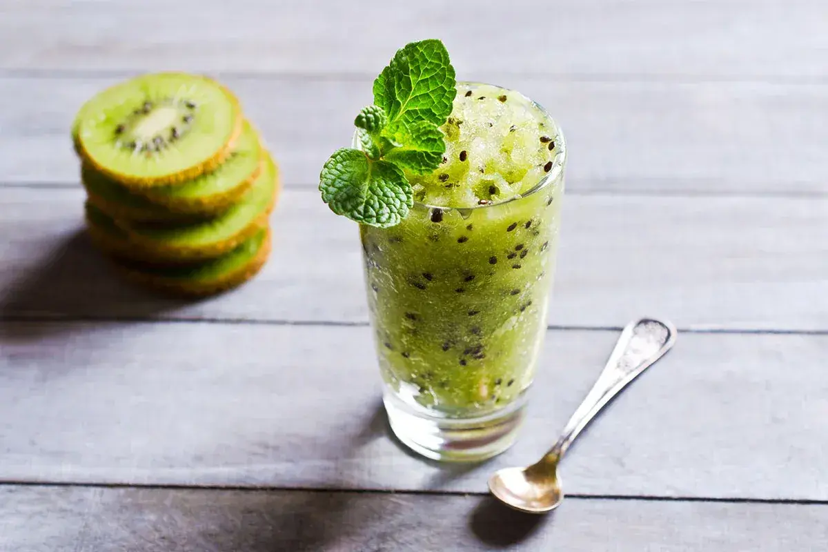 Sorbetto al kiwi rinfrescante, guarnito con menta, accanto a fette di kiwi impilate e un cucchiaino.