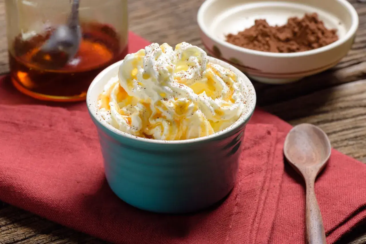 Dolcezza cremosa: cos'è heavy cream? Panna montata soffice, caramello dorato e una spolverata di cacao su un tavolo rustico.