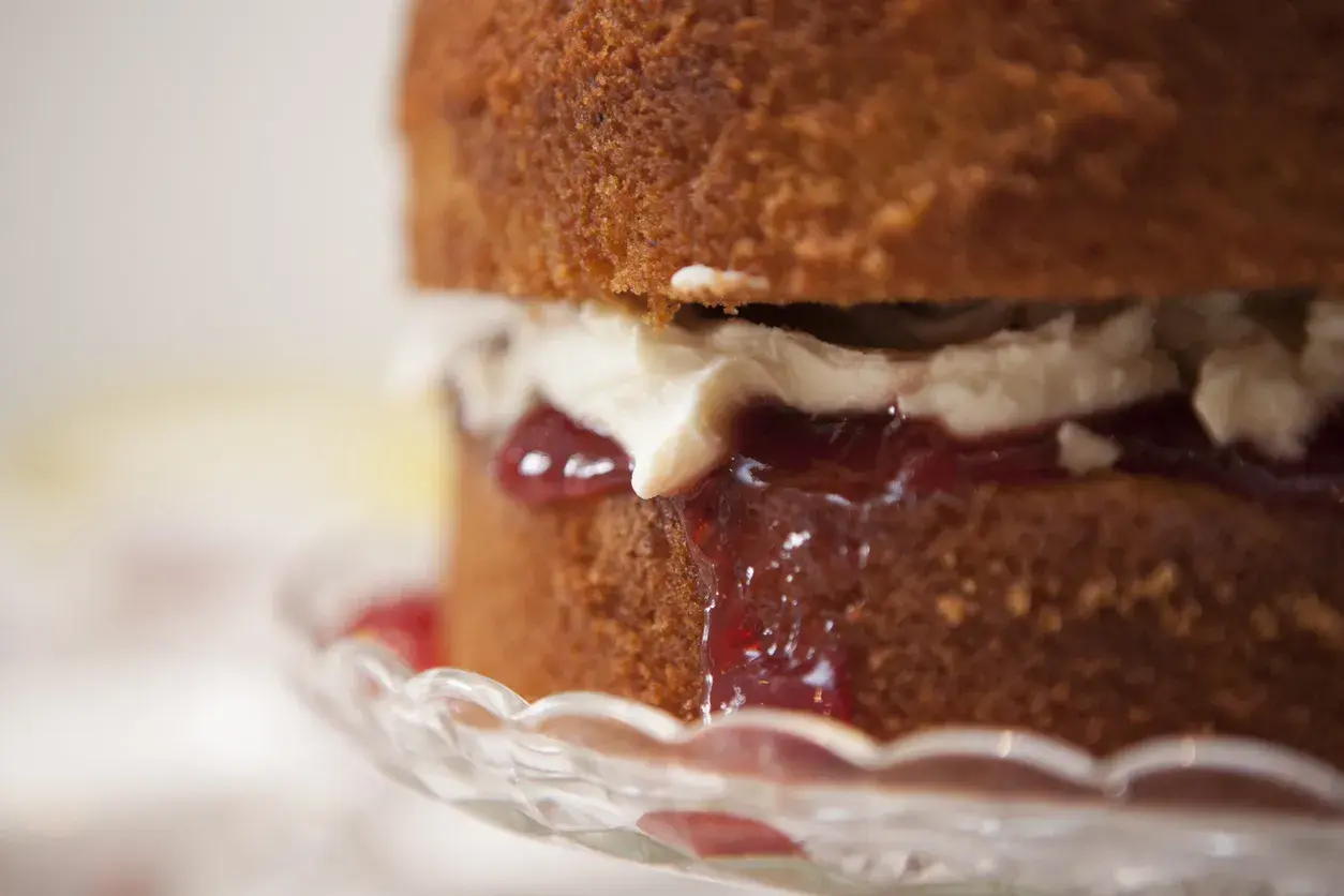 Torta soffice con panna e tanta marmellata di fragole che cola, servita su un piatto di cristallo.