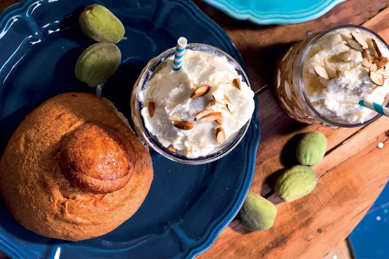 Deliziosa granita di mandorle con latte di mandorla, guarnita con mandorle a lamelle, accompagnata da un pane dolce e mandorle verdi.