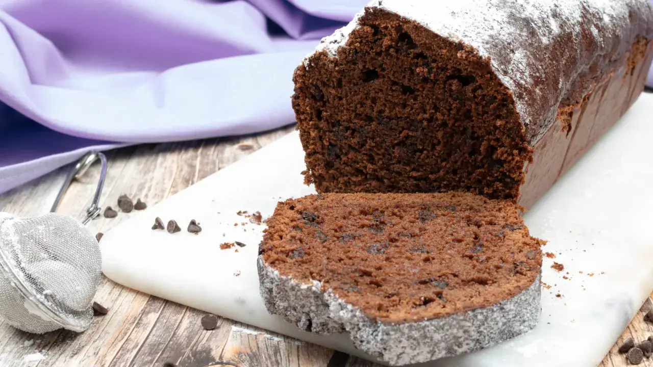 Plumcake al cioccolato soffice e goloso, spolverato di zucchero a velo, con gocce di cioccolato visibili.