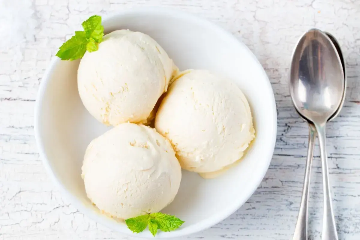 Tre palline di gelato alla vaniglia in una ciotola bianca, guarnite con menta. Perfetto per scoprire come rendere cremoso il gelato fatto in casa.