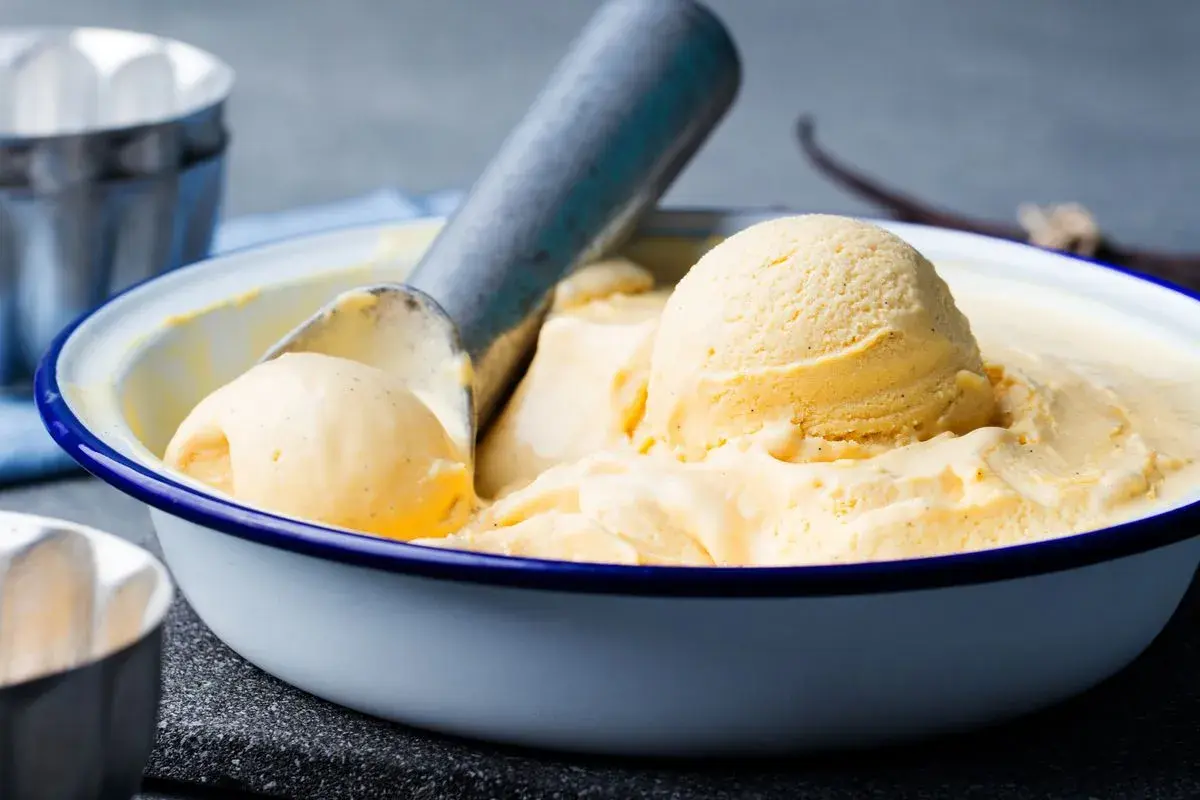 Ciotola di gelato alla vaniglia fatto in casa, con palline cremose e un mestolo. Perfetto per una calda giornata estiva.