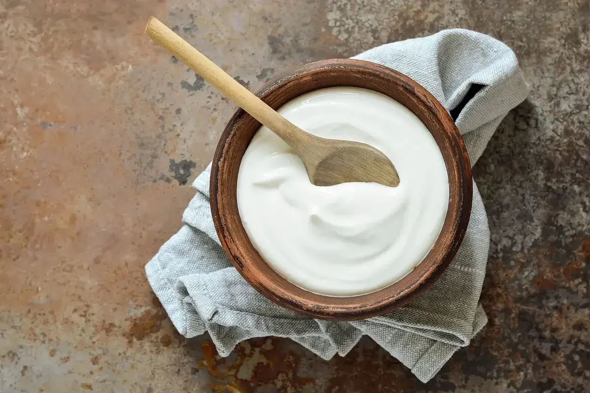 Ciotola di terracotta con panna fresca e cucchiaio di legno, un'idea su come si fa la panna da cucina in casa.