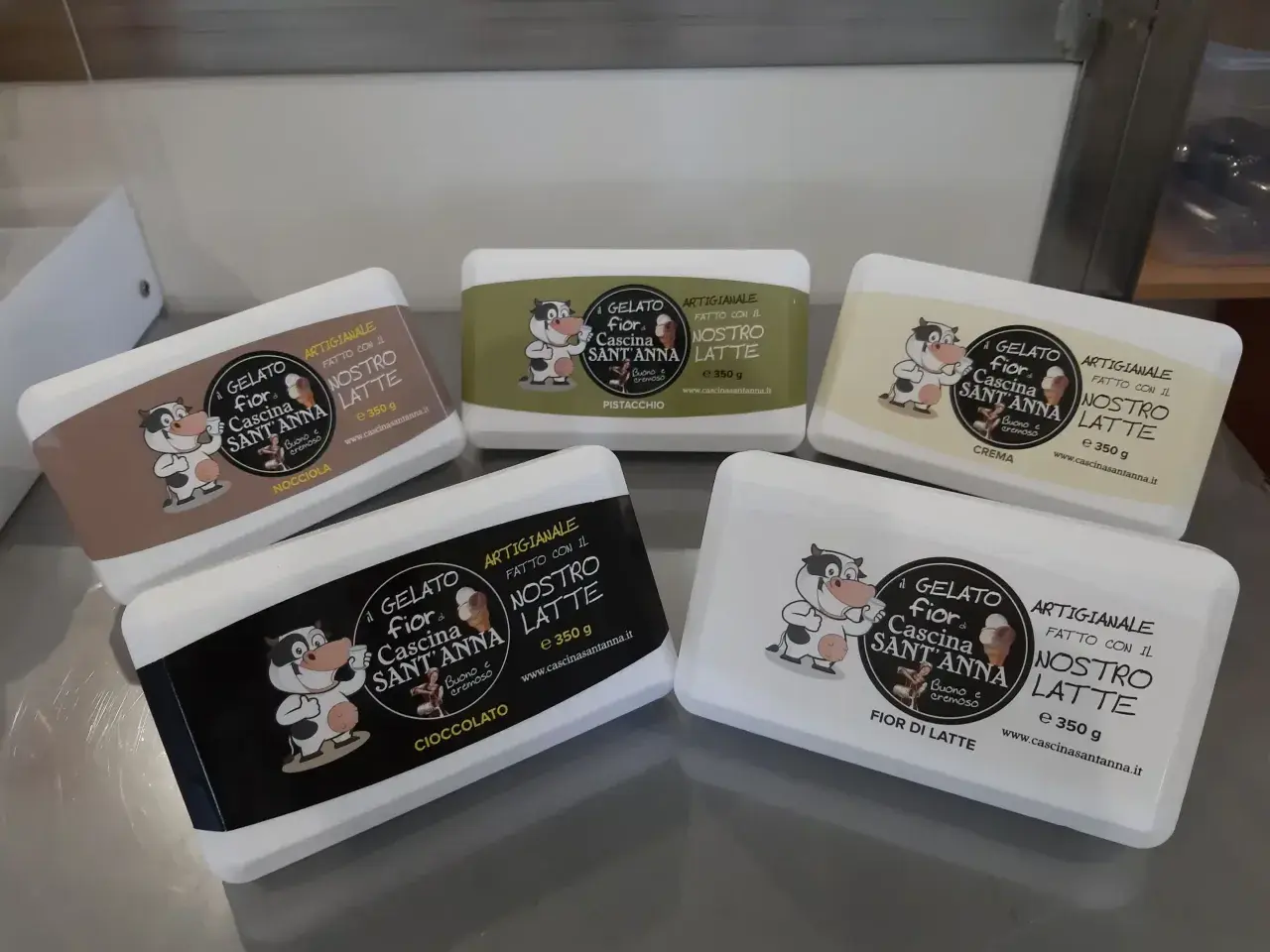 Cinque vaschette di gelato artigianale ricetta, con mucca sorridente: nocciola, pistacchio, crema, cioccolato e fior di latte.