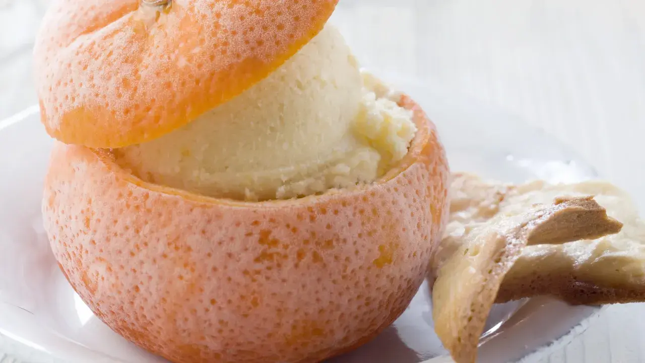 Sorbetto all'arancia servito in una scorza d'arancia ghiacciata, accompagnato da biscotti croccanti.